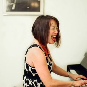 Liz Parker playing the piano and singing with a gusto.