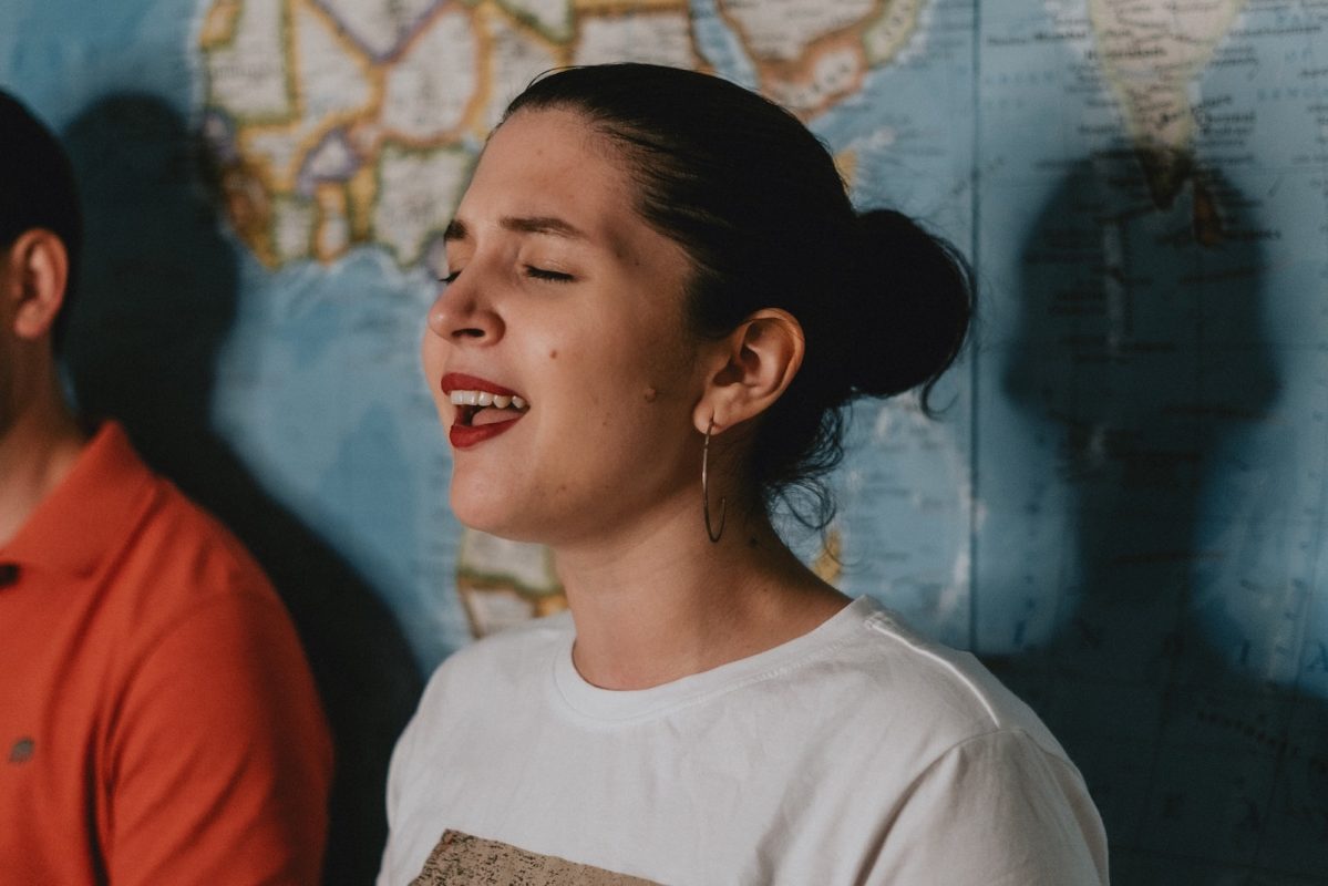 Woman singing while standing in front of a wall map of the world.